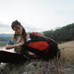 close up caucasian woman alone sitting side lake, carrying backpack